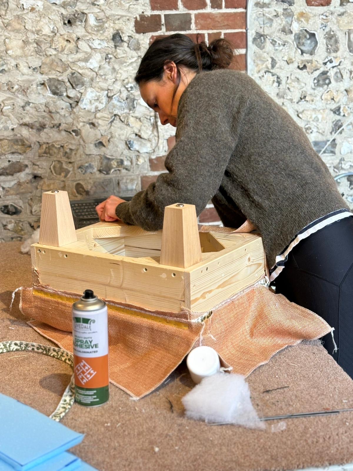A student gluing hessian onto a footstool frame at a workbench