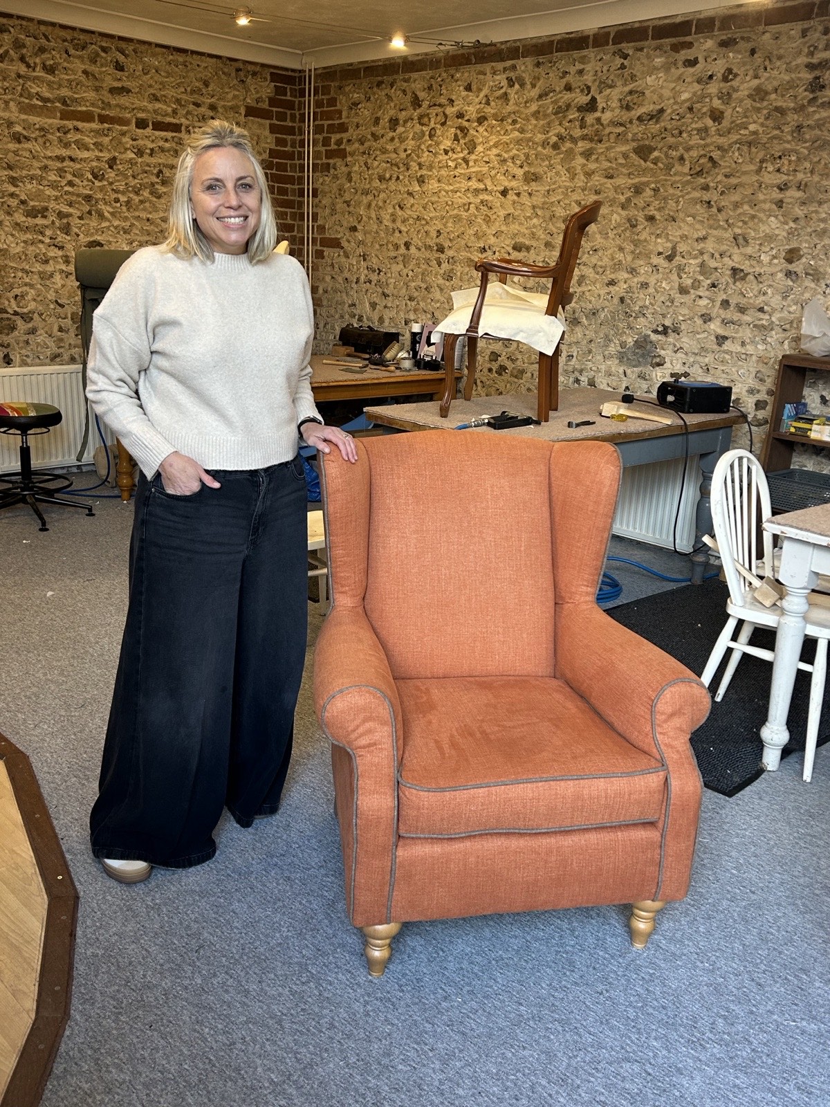 A smiling student beside her finished armchair reupholstered in coral orange fabric