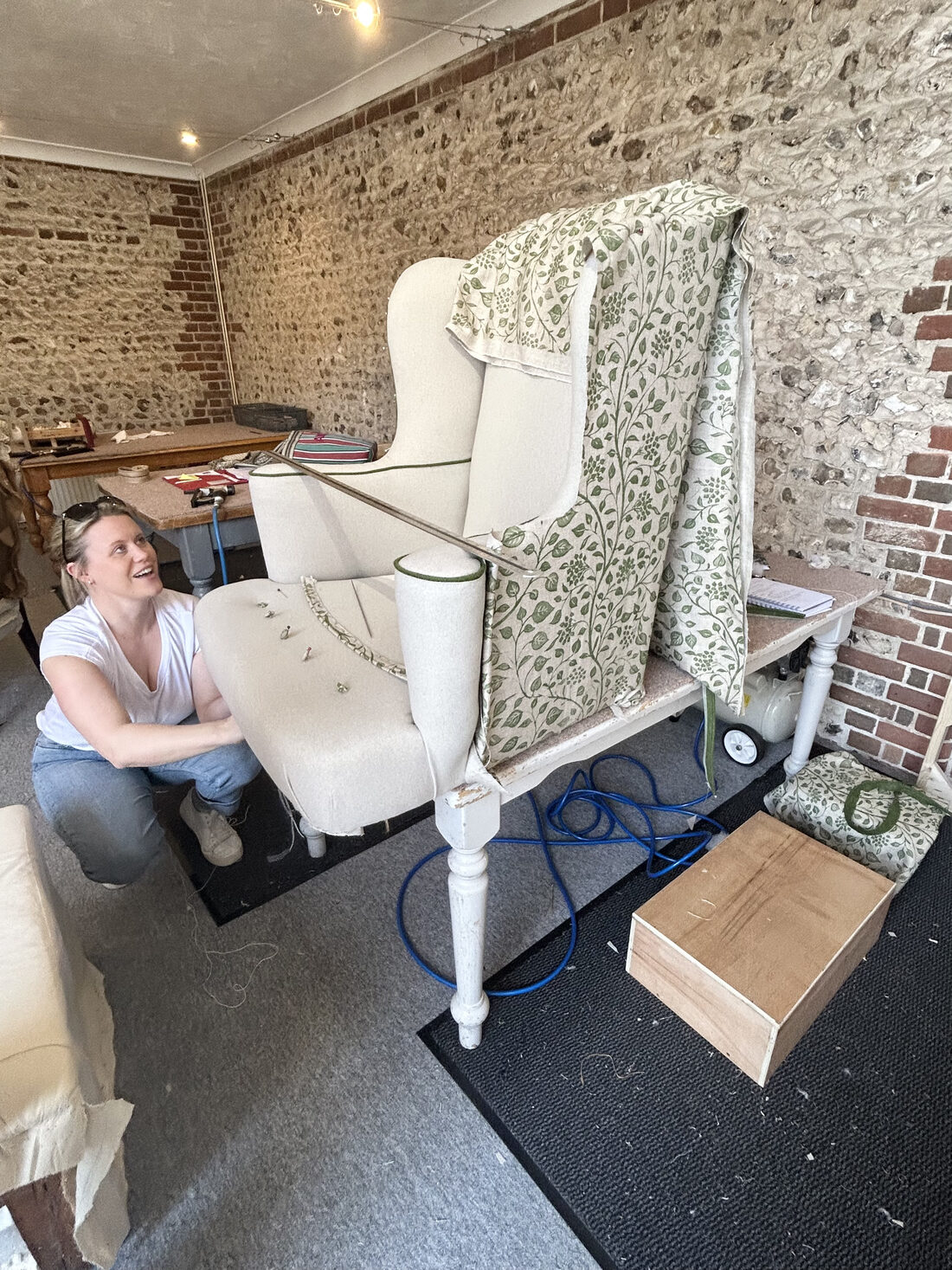 A student with a wing chair in progress in the flint-walled studio